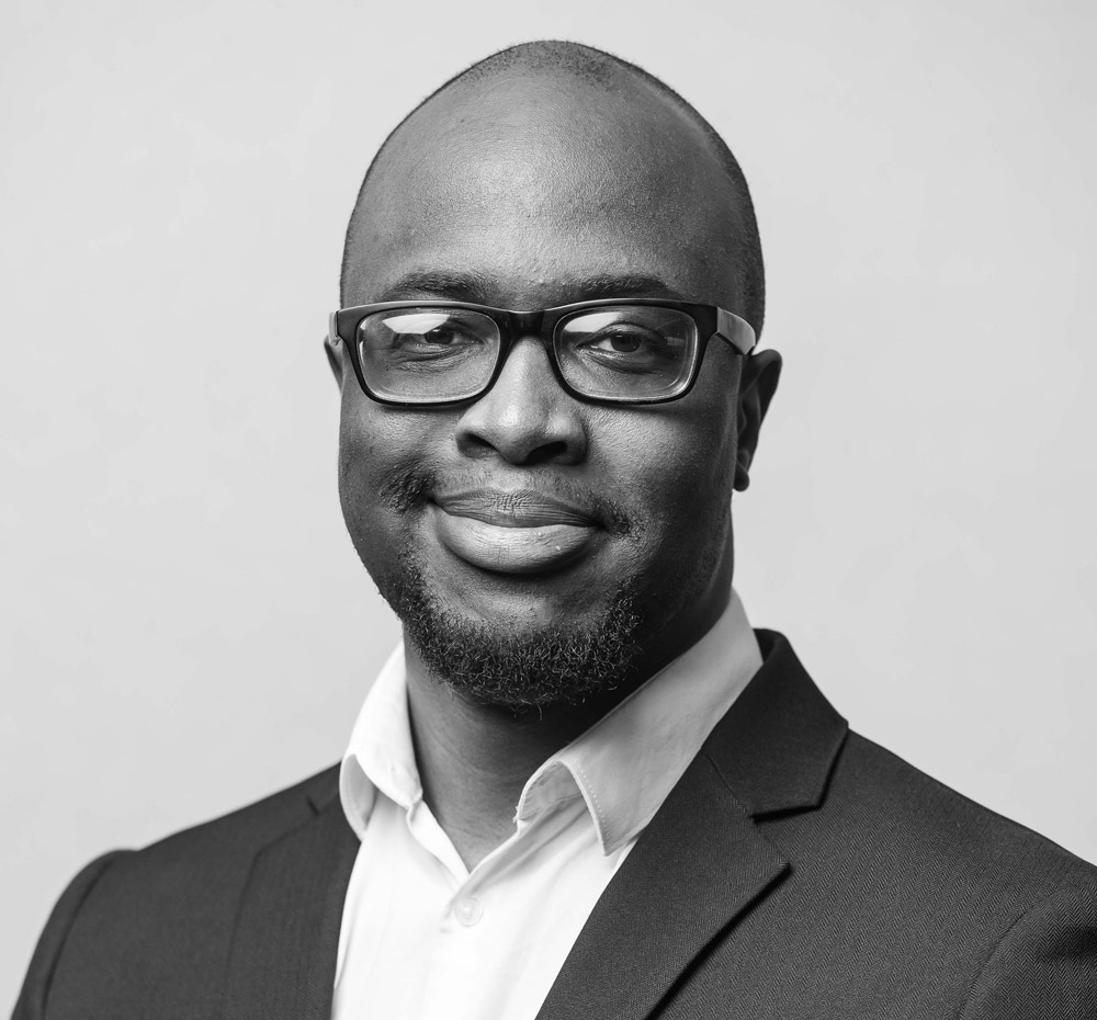 Young black man wearing a suit and glasses smiling